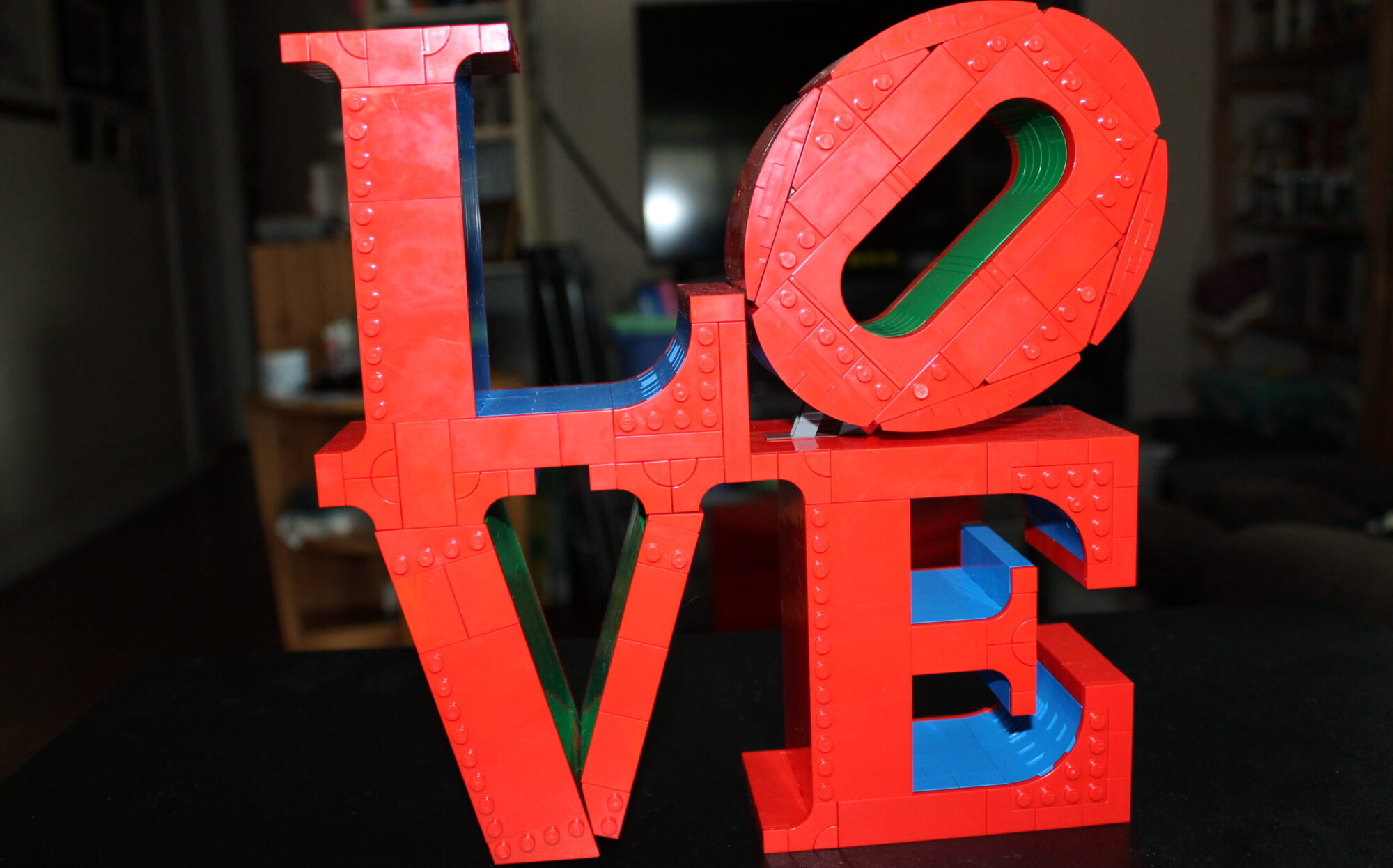 A large brick-built LEGO sculpture spelling out the word "LOVE" in a stacked design, featuring red letters with blue and green accent interiors.